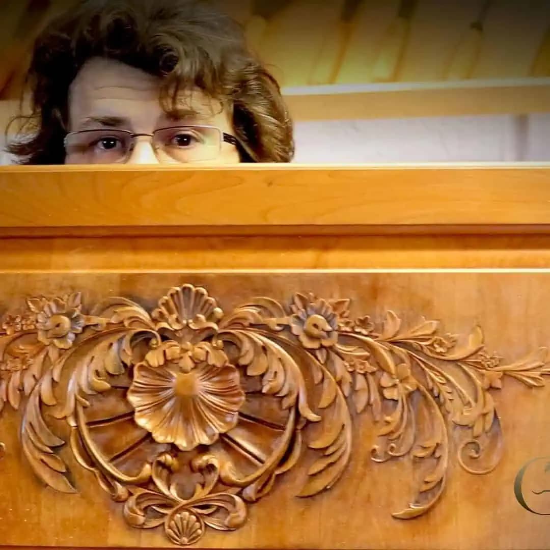 Master carver Alexander Grabovetskiy behind a custom wood carving with a central floral rosette and scrolling foliage.