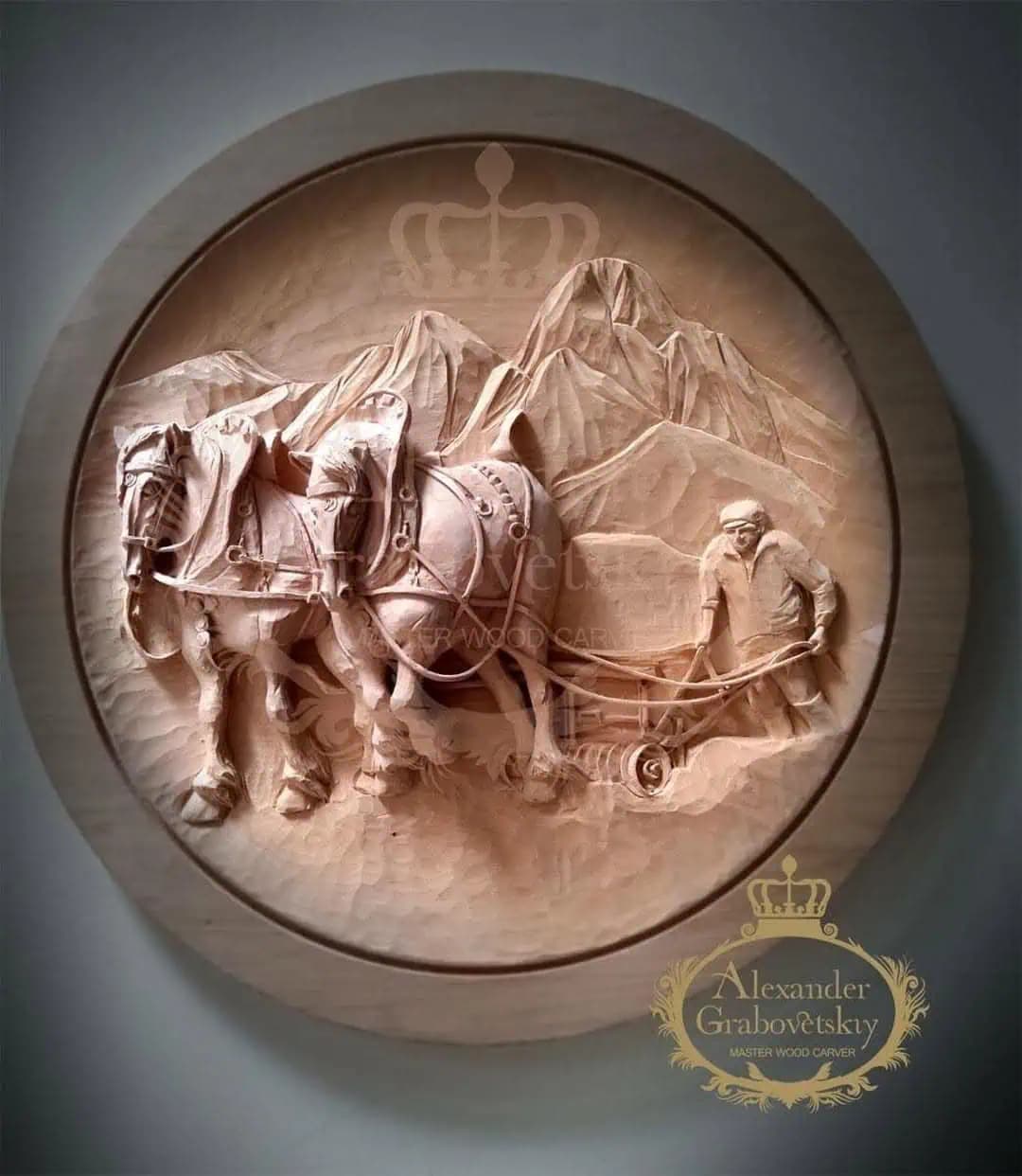 Round limewood relief of a farmer guiding two draft horses plowing before mountains, hand-carved by Alexander Grabovetskiy as custom wood carving.