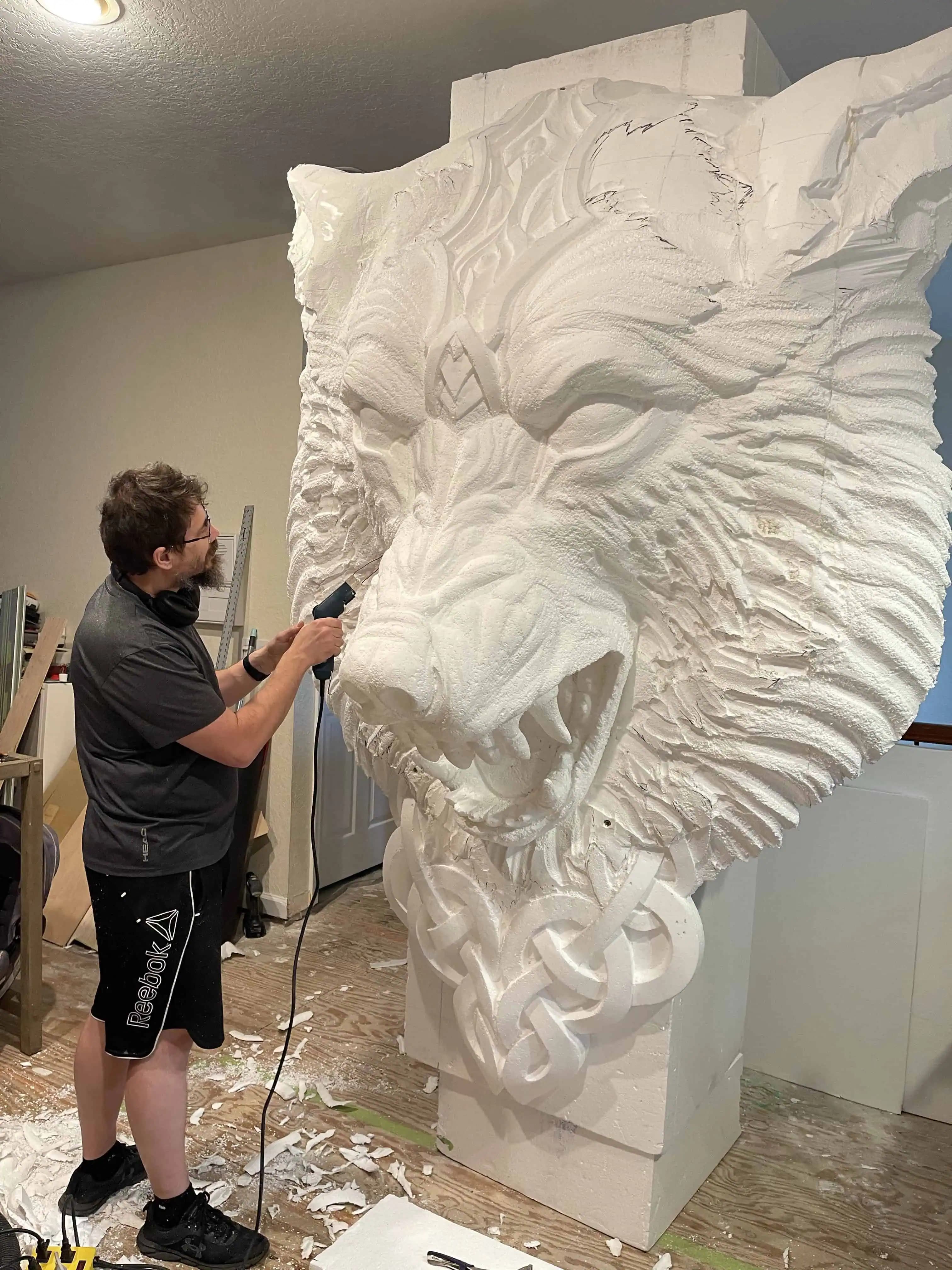 Alexander Grabovetskiy shaping a large roaring wolf head, a custom wood carving with Celtic knotwork base.
