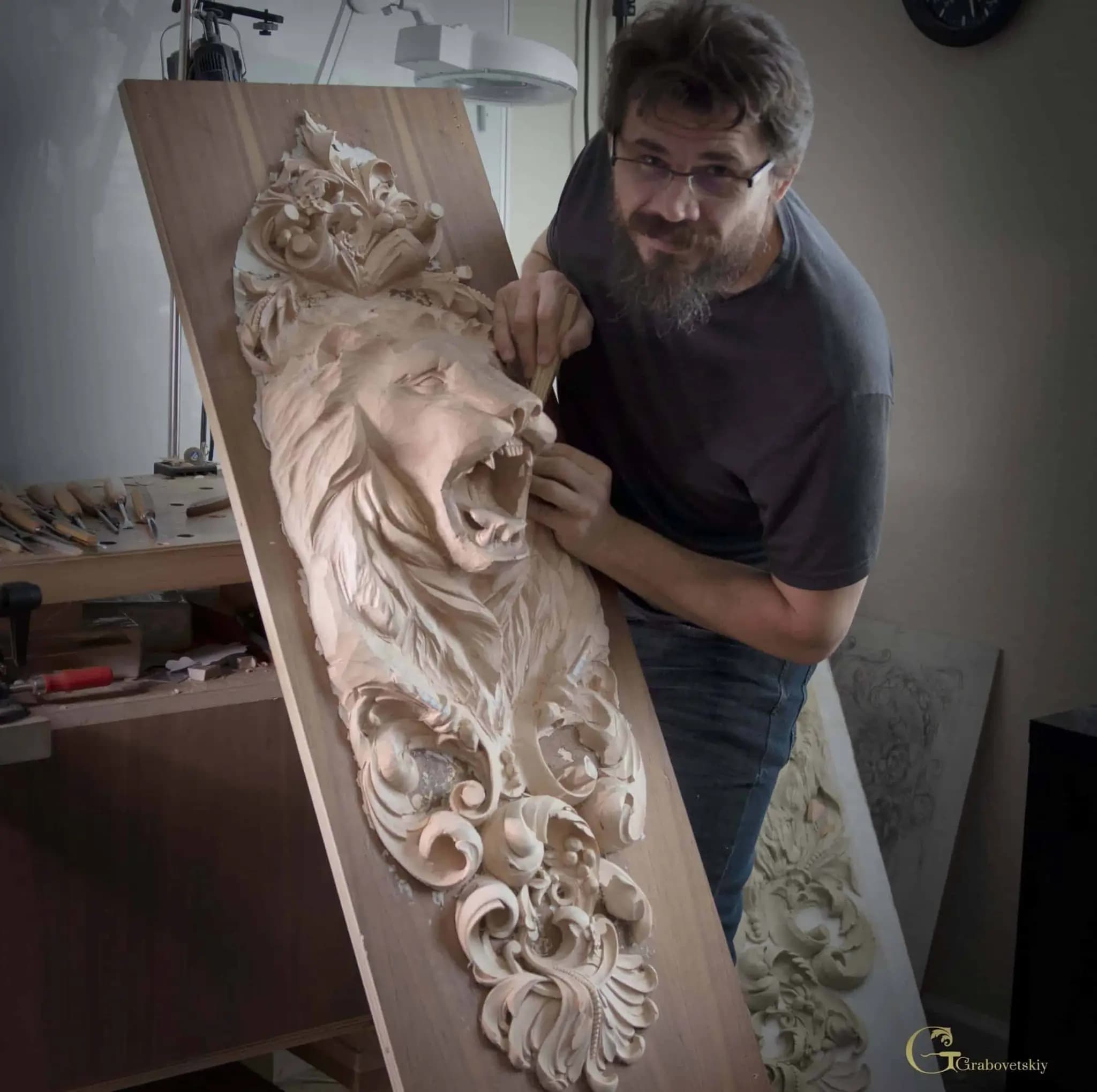 Alexander Grabovetskiy carving a roaring lion head limewood panel, a custom wood carving in progress in his studio.