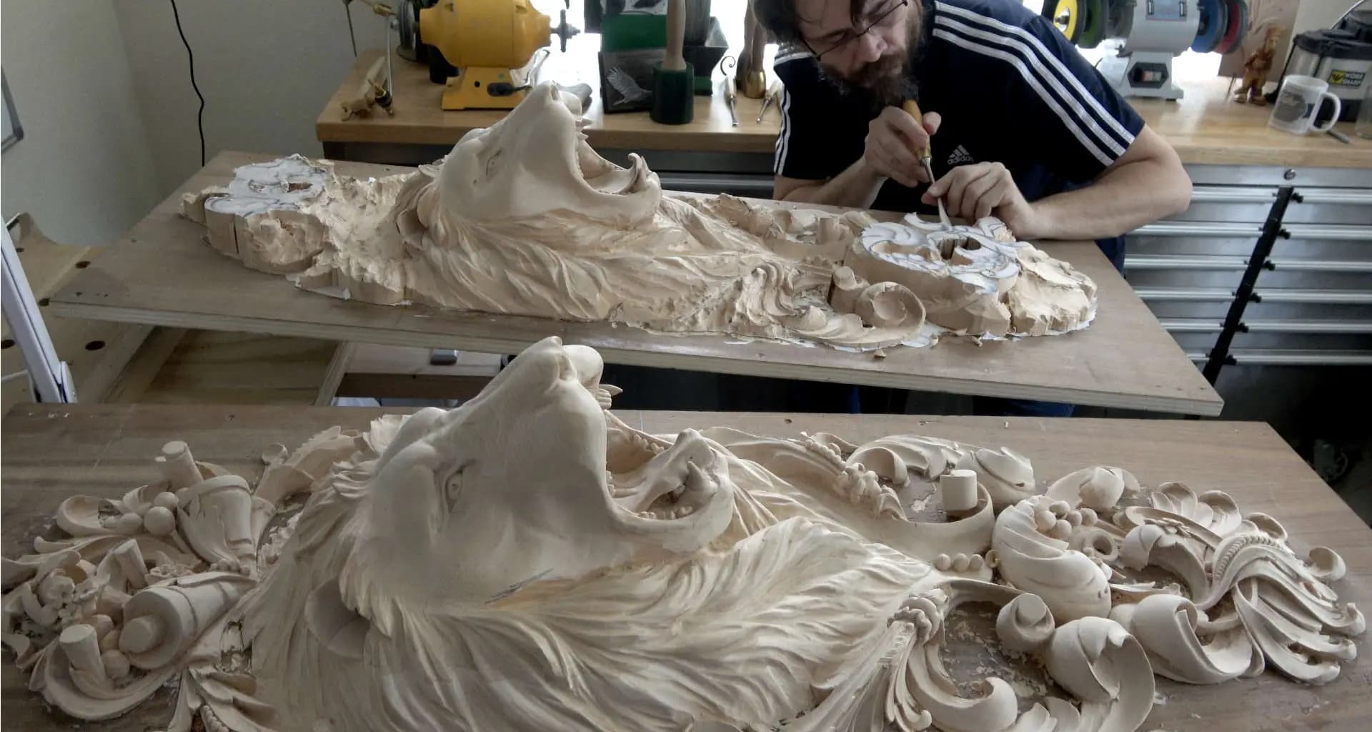 Alexander Grabovetskiy carving two roaring lion heads in limewood, a custom wood carving in progress.
