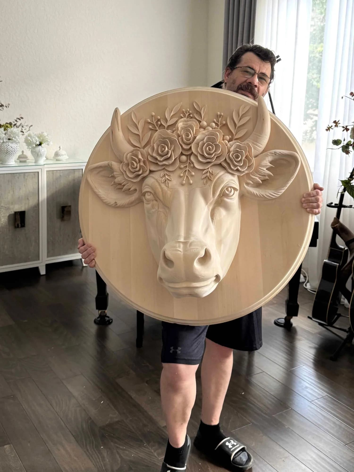Die Besoffene Kuah (The Drunk Cow) Alexander Grabovetskiy holds Die Besoffene Kuah, a round custom wood carving of a cow's head with roses between the horns. It is American basswood, 36 inches across, made for a winery in Austria.